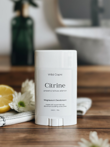 Wild Capri Citrine magnesium deodorant on a wooden surface with lemons and flowers in the background