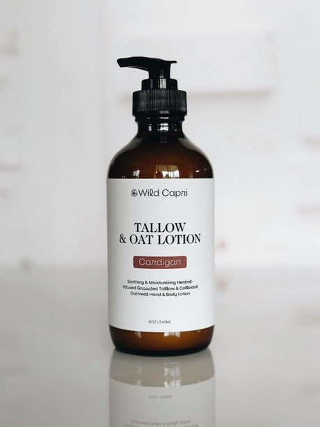 A bottle of Wild Capri Tallow & Oat Lotion in the Cardigan scent, featuring an amber glass bottle with a black pump and a white label, set against a bright, softly blurred background.
